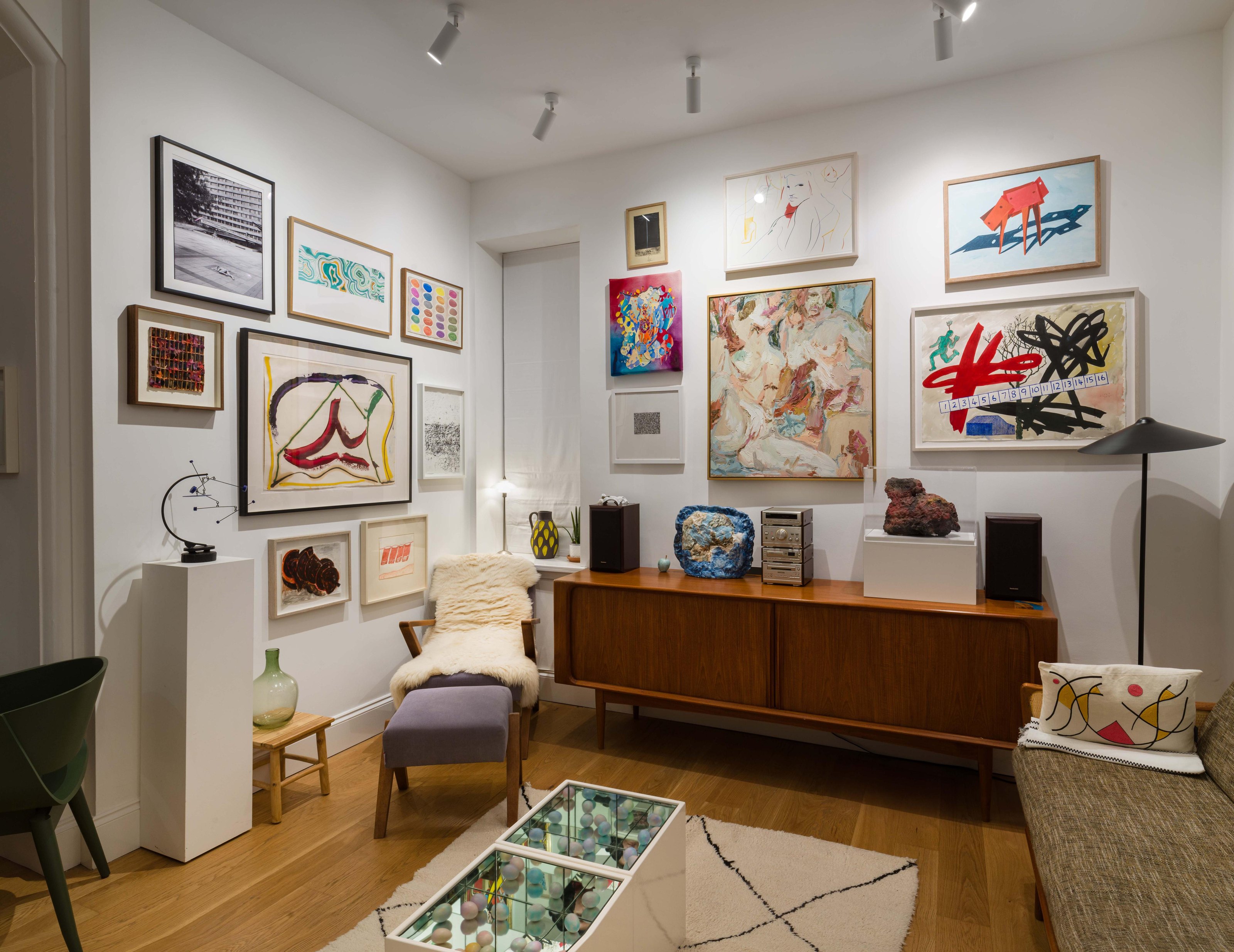A room in the Joseph Clark Collection hung salon-style: framed paintings, drawings and photographs cover two white walls, with sculptures on a teak sideboard and a white plinth below.